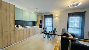 A modern kitchen with wooden cabinets, a dining area with a glass table and chairs, and a living area with a sofa and large windows. - Casa Rigola El Cotillo (El Cotillo)