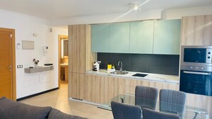 A modern kitchen with wooden cabinets, a built-in oven, and a glass dining table. - Casa Rigola El Cotillo (El Cotillo)