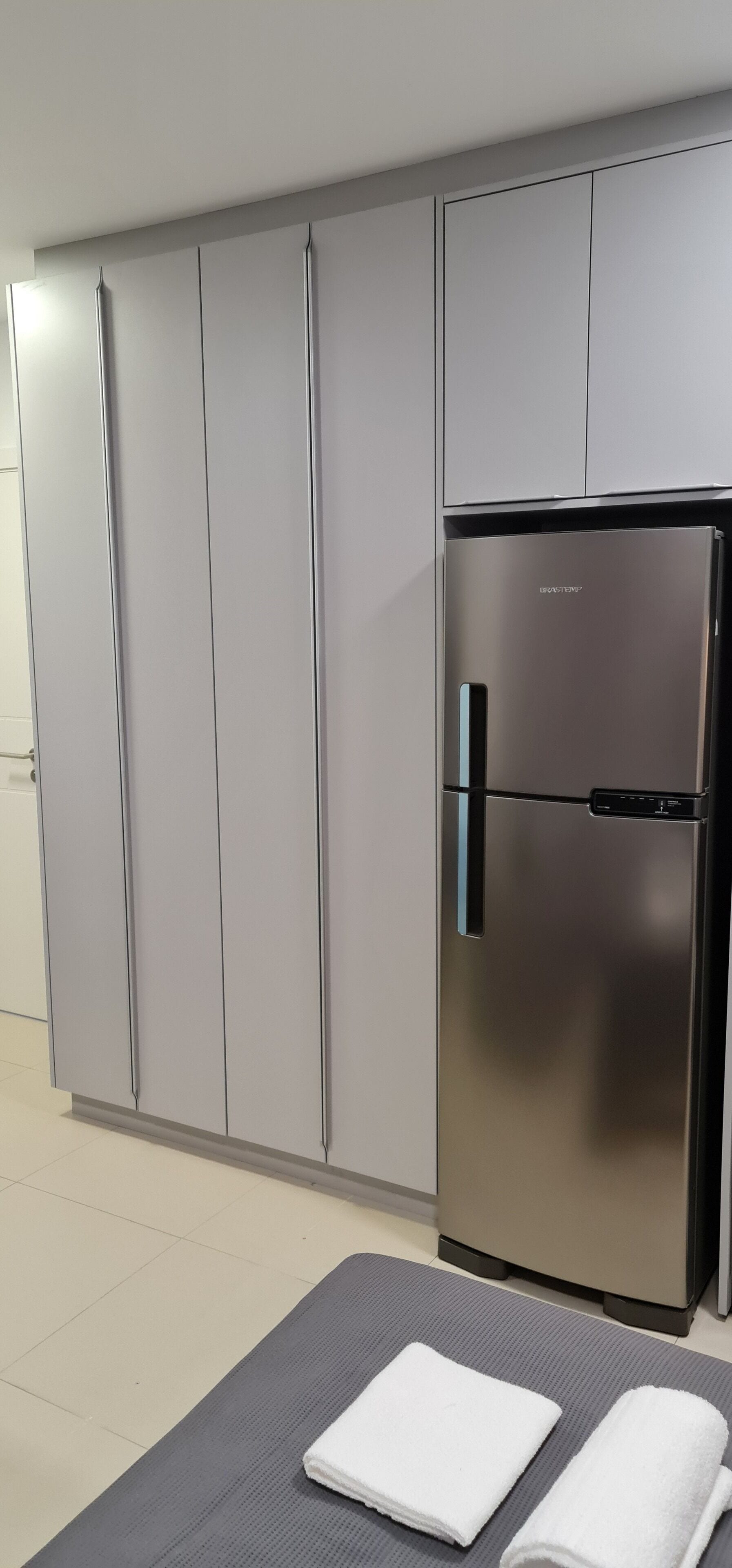 A modern kitchen with grey cabinets, a stainless steel refrigerator, and a grey mat with towels.