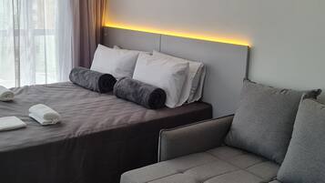 Habitación de hotel con una cama bien hecha, un sofá y un cabecero con iluminación integrada.