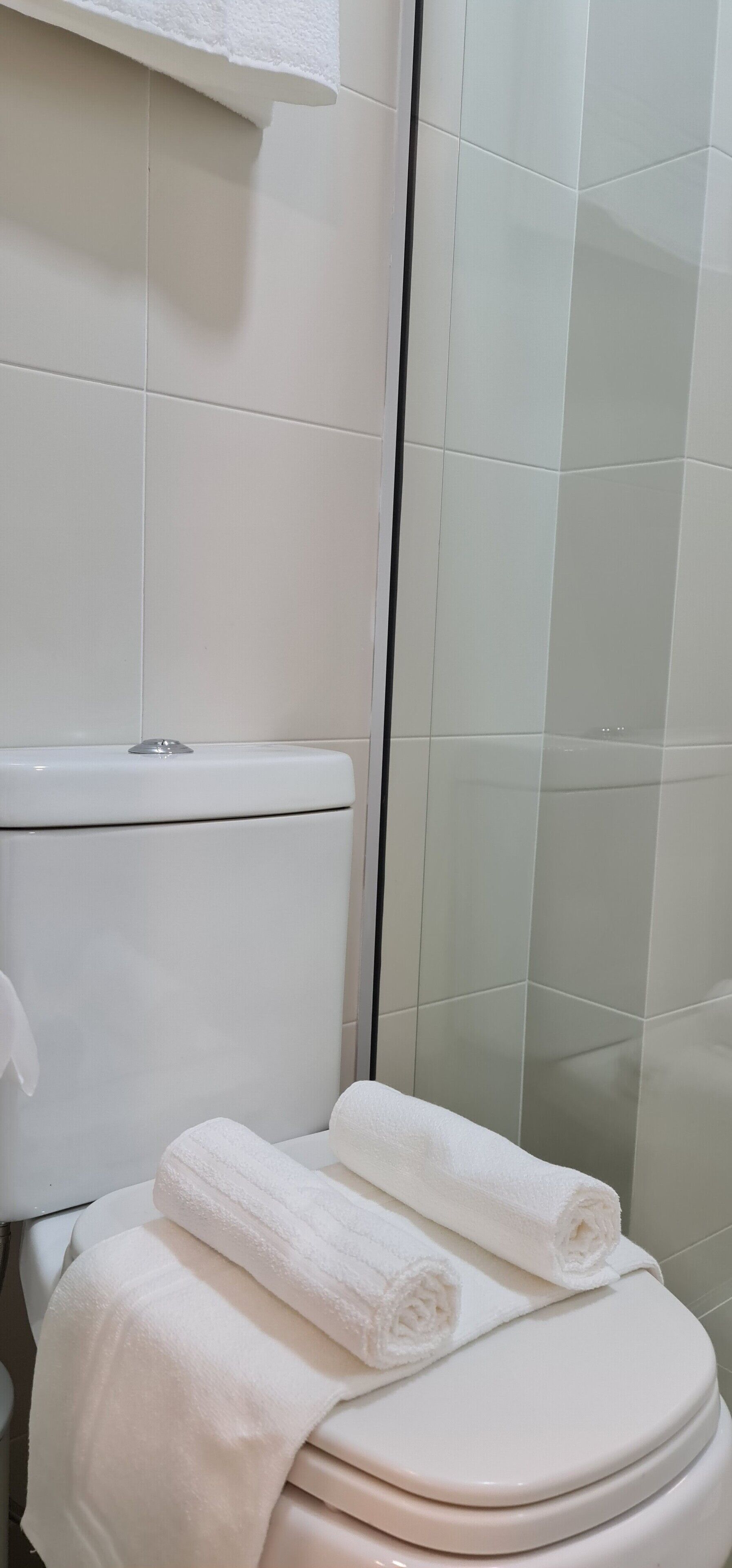 A bathroom with a toilet, a glass shower enclosure, and a stack of white towels on the toilet seat.