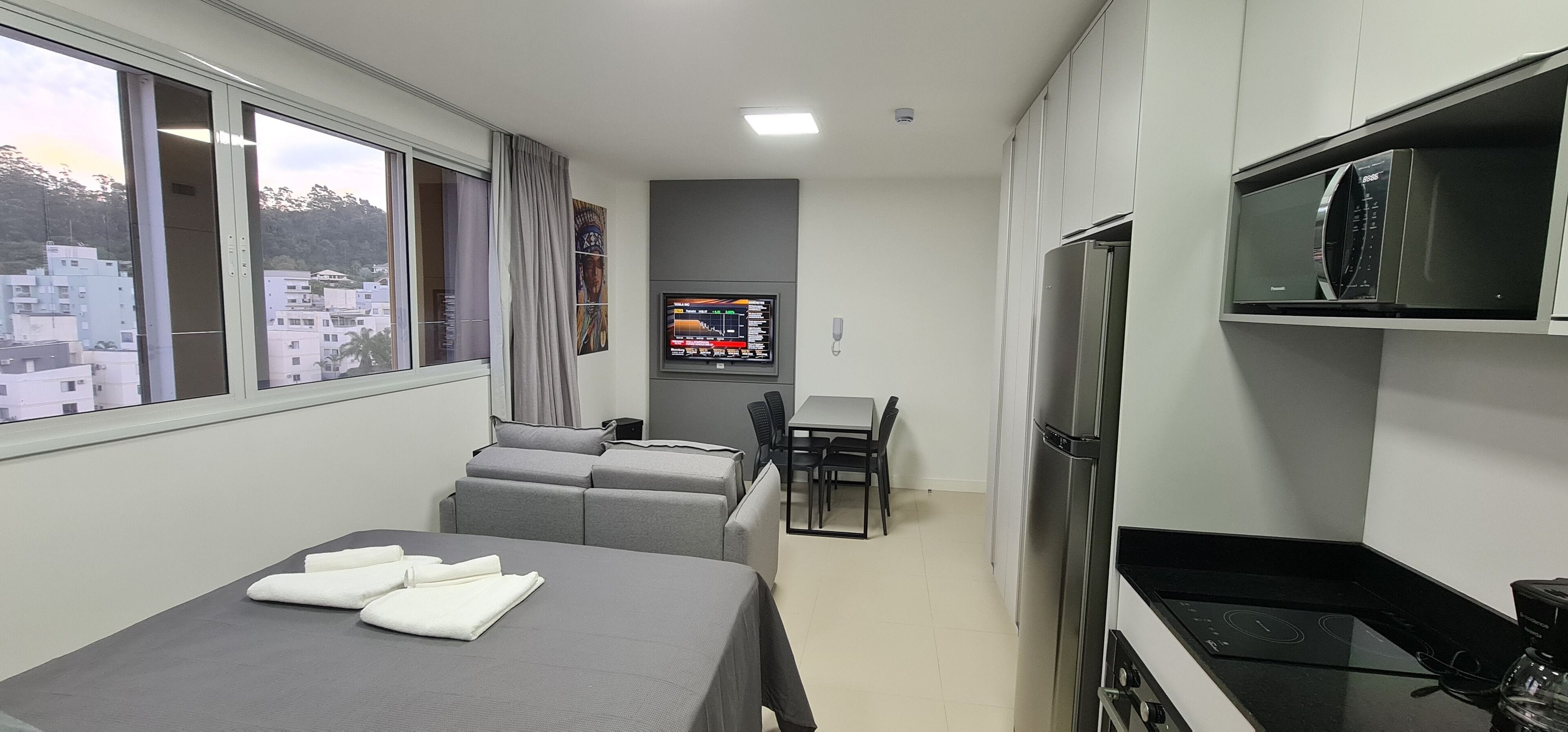 Egy modern szállodai szoba, amelyben található egy ágy, egy kanapé, egy étkezőasztal és egy kis konyhasarok.