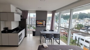 Une cuisine moderne avec un coin repas, un téléviseur affichant les données du marché boursier et un balcon offrant une vue sur la ville.