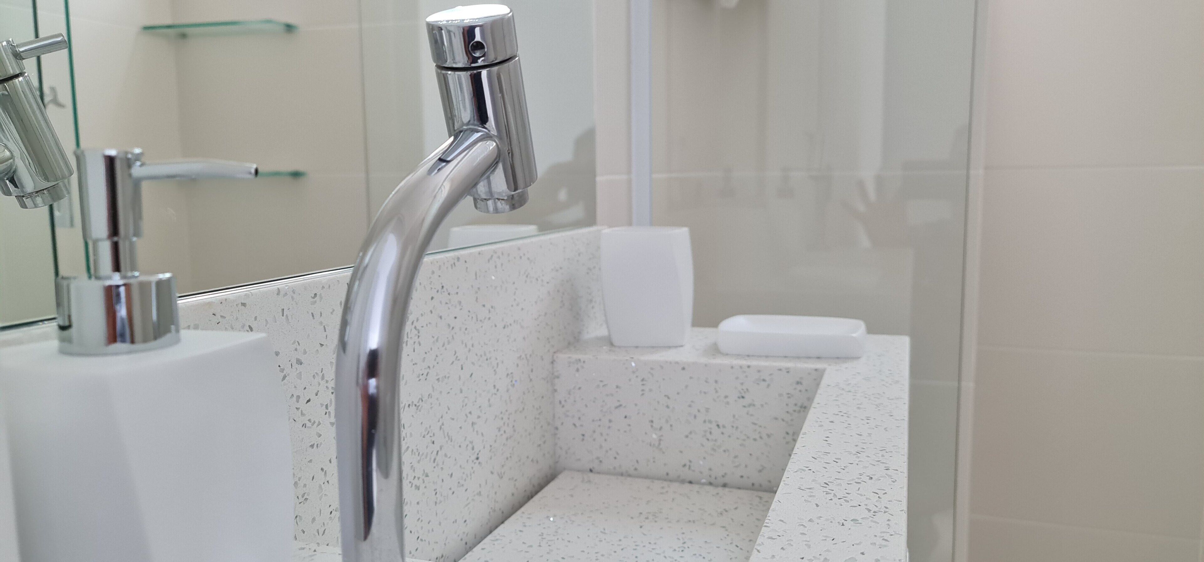 A modern bathroom with a chrome faucet, a glass shower enclosure, and a white sink.