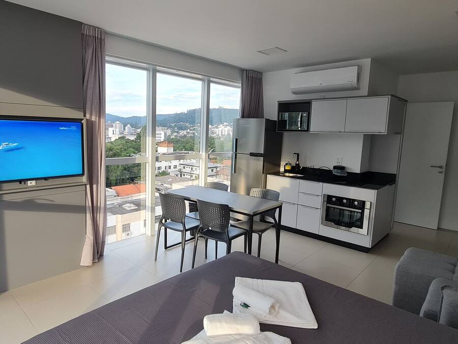 Una habitación de hotel moderna con un ventanal grande, televisión de pantalla plana, zona de comedor y kitchenette.