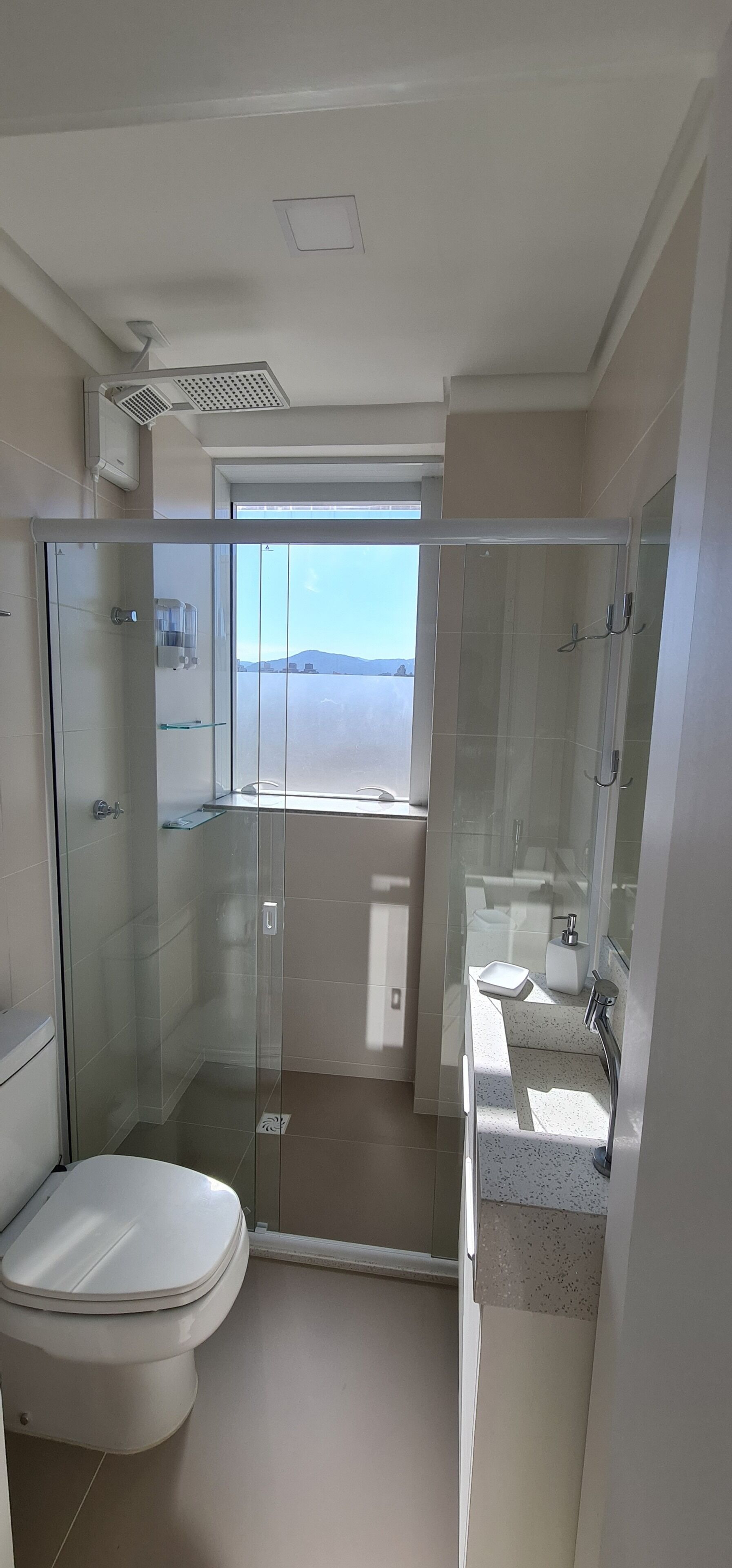 Un baño moderno con ducha de vidrio, inodoro y lavamanos con espejo.