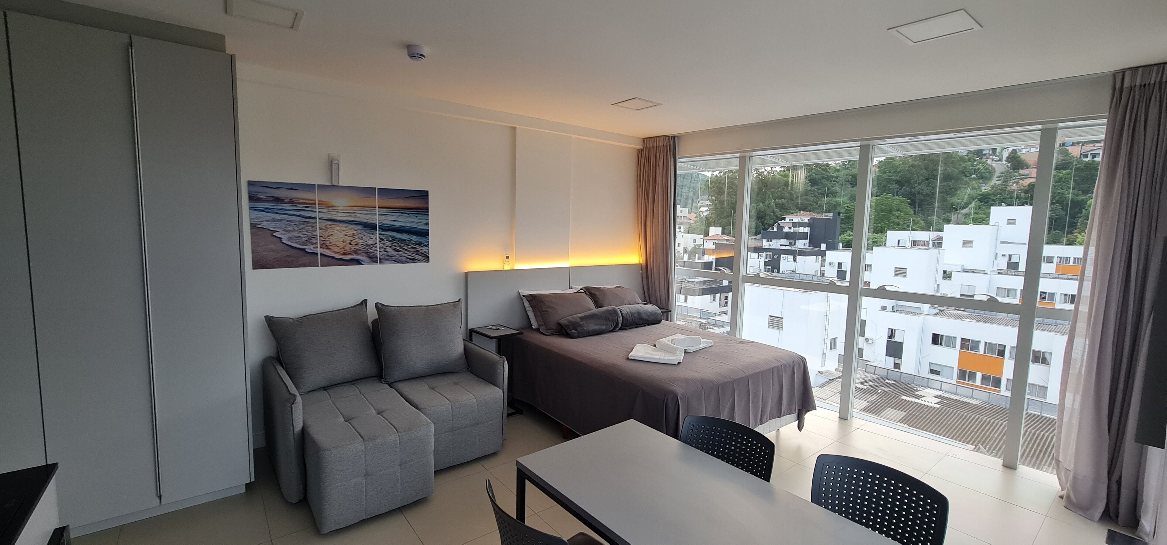 Een moderne hotelkamer met een bed, een slaapbank, een eettafel en een groot raam met uitzicht op de stad.