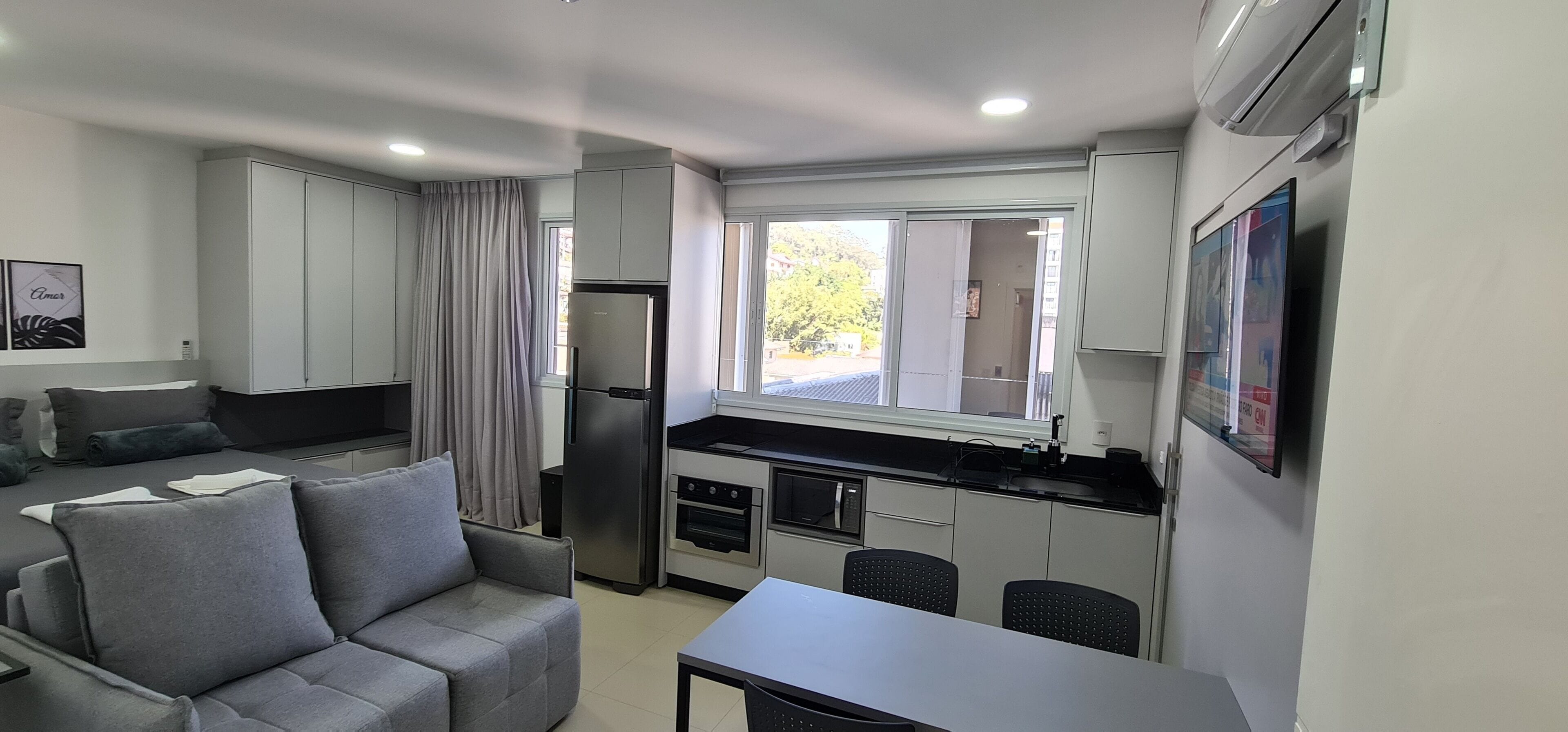 A compact living space with a kitchenette, a sofa, a dining table, and a TV mounted on the wall.