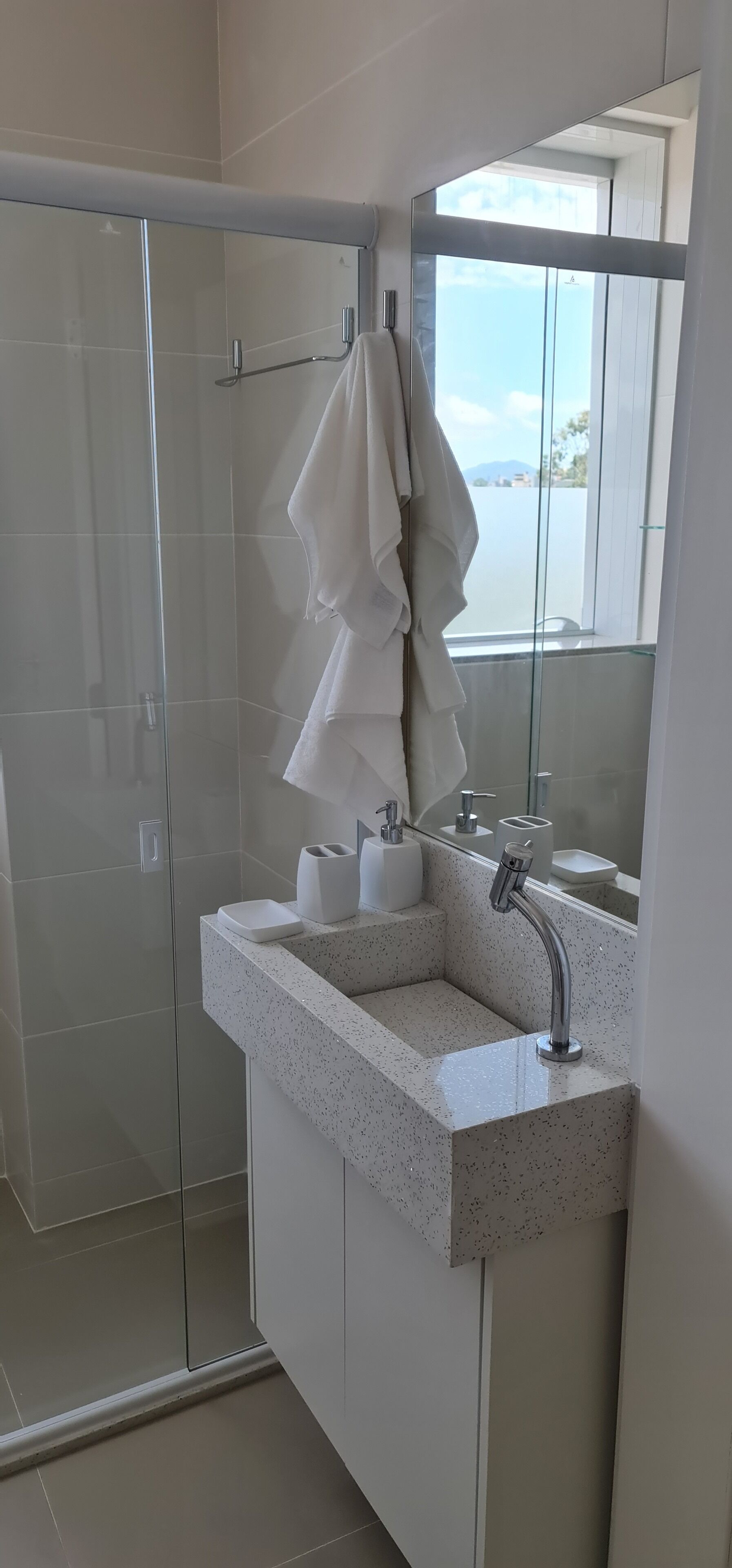 Uma casa de banho moderna com cabine de duche em vidro, um espelho grande e lavatório com produtos de higiene pessoal.