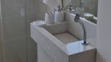Uma casa de banho moderna com cabine de duche em vidro, um espelho grande e lavatório com produtos de higiene pessoal.