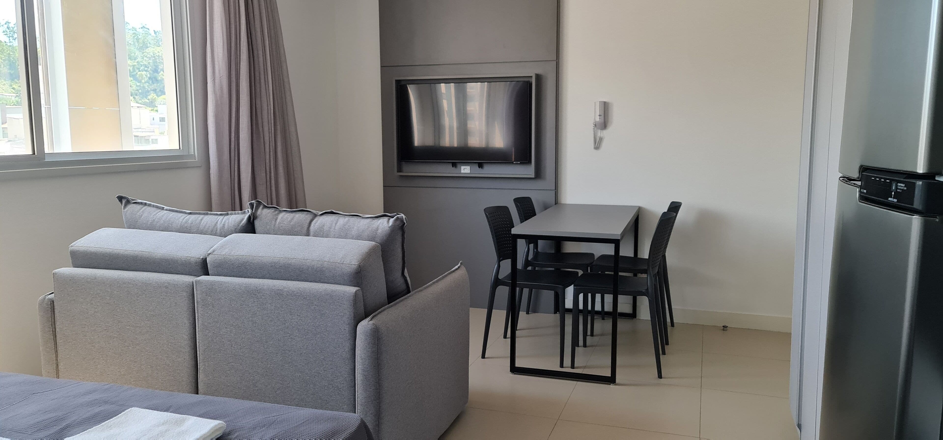 A modern room with a sofa, a TV mounted on the wall, a dining table with chairs, and a refrigerator.
