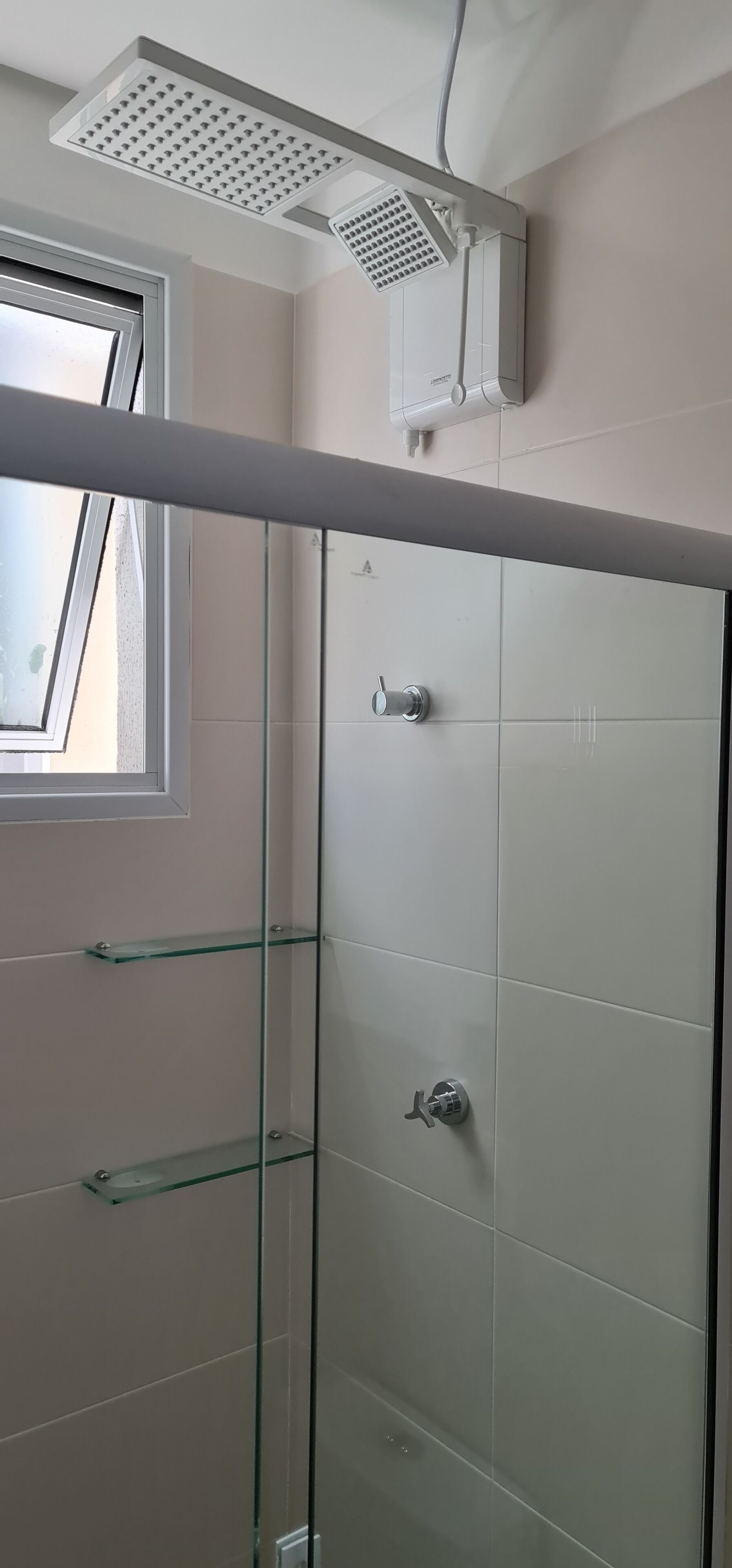 Een glazen douchecabine met een in het plafond gemonteerde regendouche, een raam en een betegelde wand.