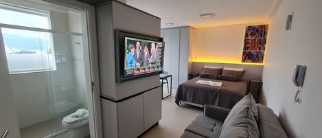 Une chambre d’hôtel compacte comprenant un lit, un canapé, un téléviseur fixé à un meuble, une douche en verre et une vue sur la mer.