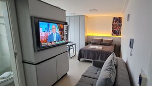 Une chambre d’hôtel moderne équipée d’un lit, d’un canapé, d’un téléviseur diffusant une chaîne d’information et d’une œuvre d’art accrochée au mur.