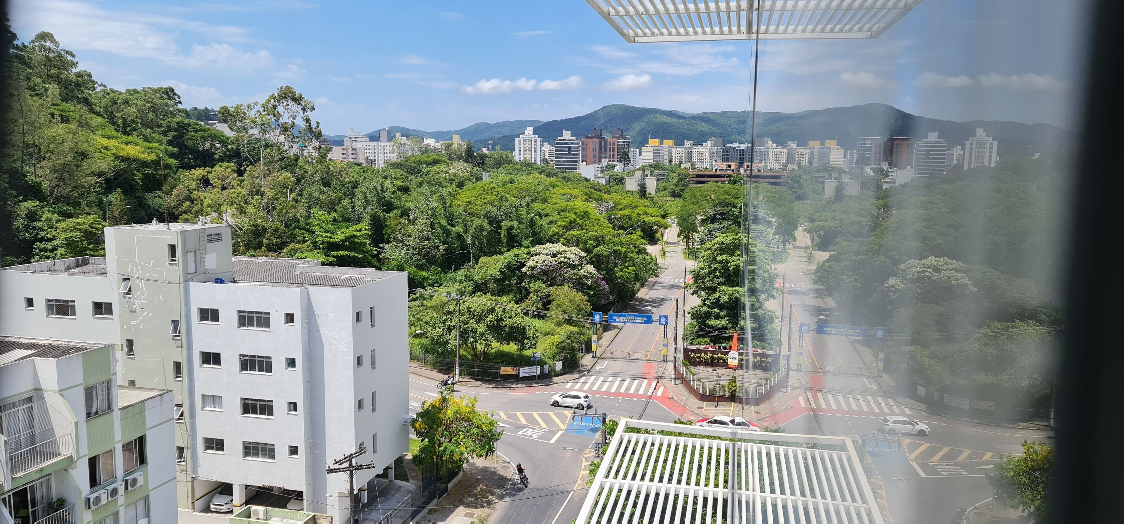 Un paisaje urbano con edificios modernos, una carretera con vehículos y una colina verde al fondo.