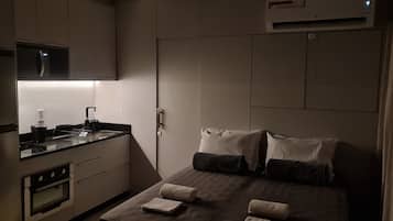 Una camera d'albergo compatta con angolo cottura, un letto con cuscini e una tenda.