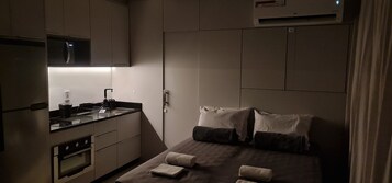 Una camera d'albergo compatta con angolo cottura, un letto con cuscini e una tenda.