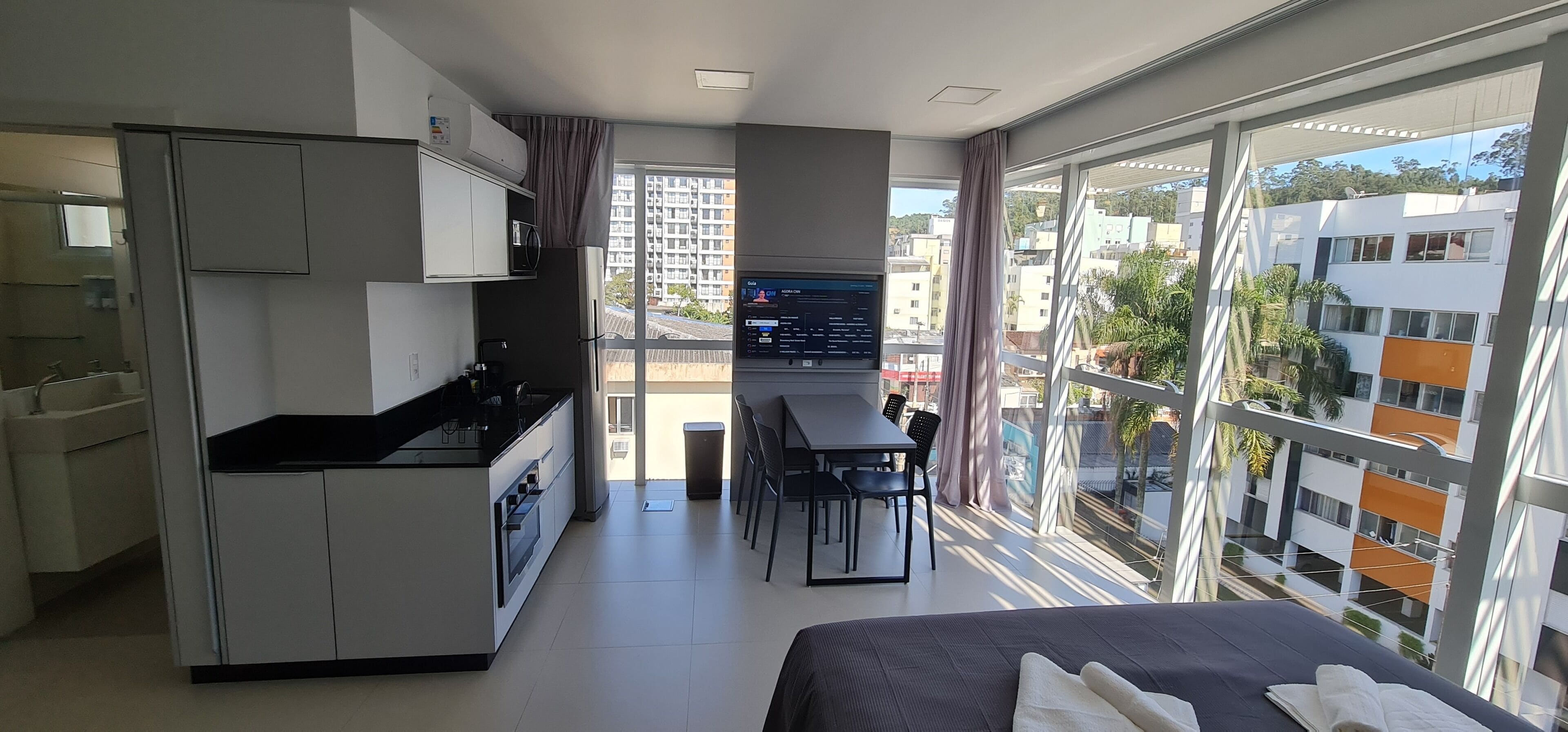 A modern apartment with a kitchenette, dining area, and a large window with a city view.