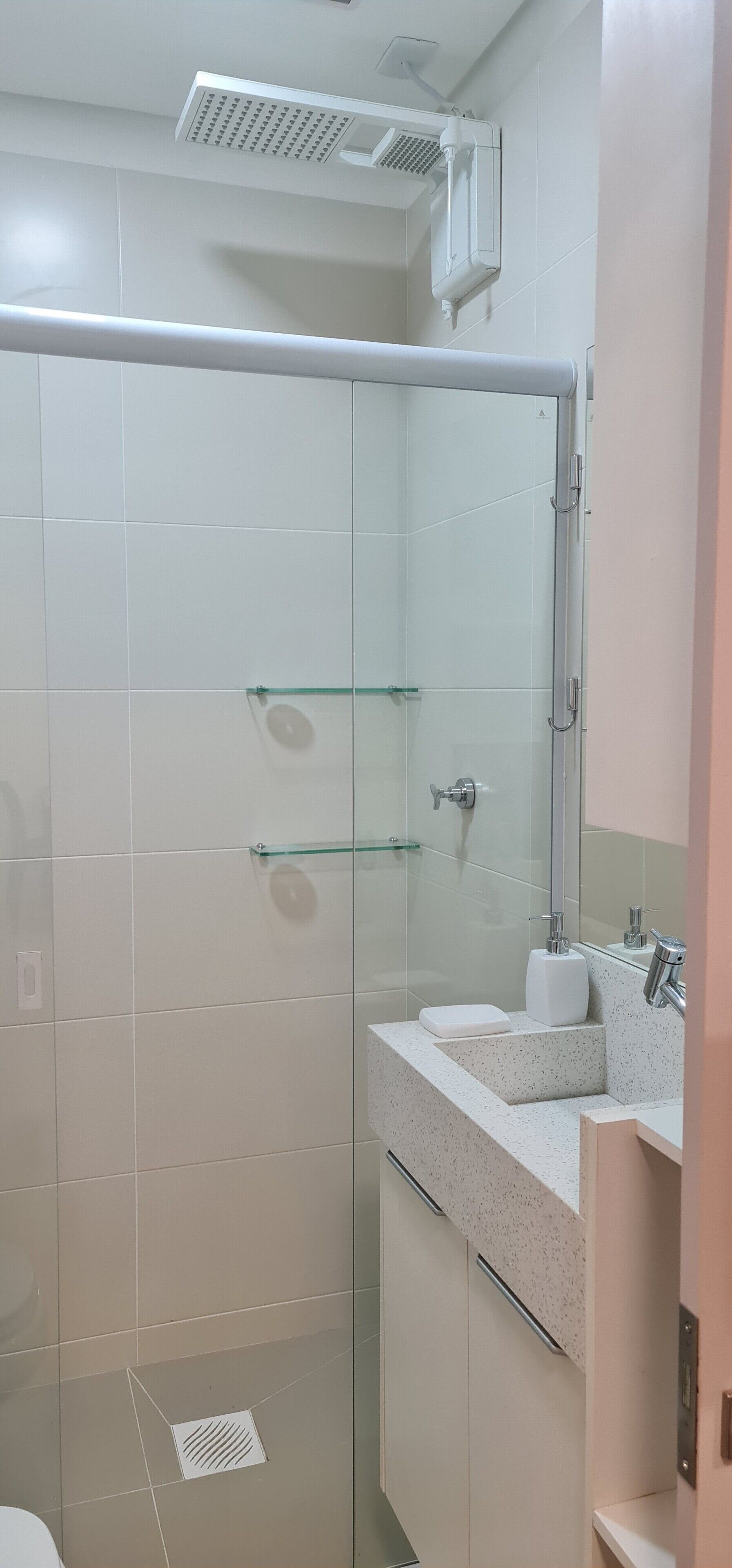Ein modernes Badezimmer mit einer Duschkabine, einer Glasablage, einem Waschbecken mit Seifenspender und einem Spiegel.