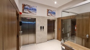 Un espace moderne pour les ascenseurs, comprenant deux ascenseurs, une cloison en verre et des œuvres d’art sur les murs.