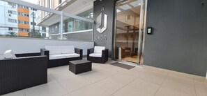 A modern outdoor seating area with wicker furniture and a glass door entrance. - AZZA Smart Stay (Florianópolis)