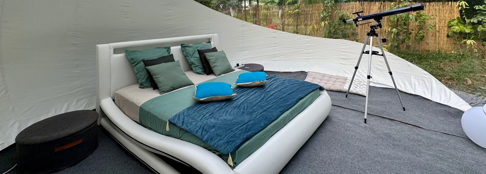 Une pièce aménagée avec une tente, un lit, des oreillers, une couverture et un télescope.