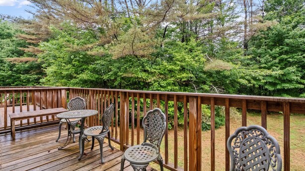 Eine Holzterrasse mit Metallstühlen und einem Tisch, umgeben von üppiger Vegetation und Bäumen.