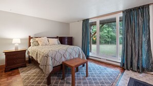 Ein Schlafzimmer mit einem Bett, einem Nachttisch, einer hölzernen Bank und einer großen Schiebeglasdoor, die zu einem Garten führt.