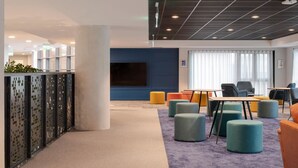 A modern office space with a large TV screen, colorful seating, and a grid-patterned ceiling. - Aspen House - Campus Accommodation (Dublin)
