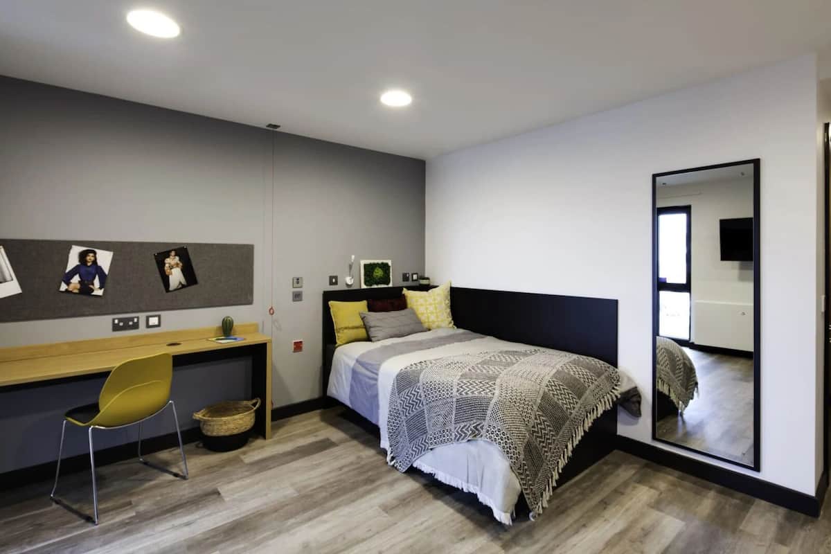 A modern bedroom with a bed, a desk, a chair, and a large mirror.