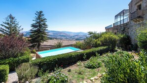 A swimming pool surrounded by lush greenery and a stone building with a balcony. - Dependance a Baglio il Corvo by Wonderful Italy (Geraci Siculo)