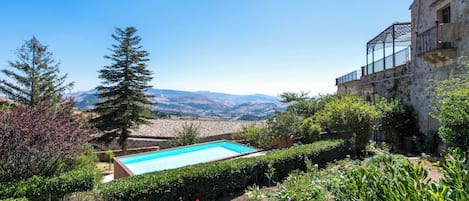 A swimming pool surrounded by lush greenery and a stone building with a balcony.