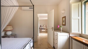 A bedroom with a four-poster bed, a bedside table with a lamp, a dresser, and a window with a view of the outside. - Dependance a Baglio il Corvo by Wonderful Italy (Geraci Siculo)