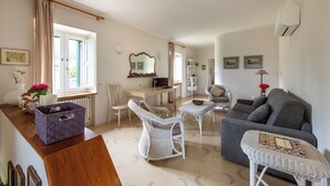 A spacious living room with a grey sofa, white wicker chairs, and a small table. A dining area with a table and chairs is visible in the background. - Dependance a Baglio il Corvo by Wonderful Italy (Geraci Siculo)
