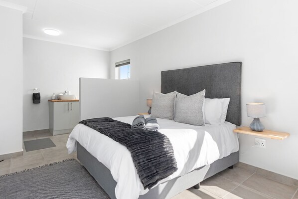 A modern bedroom with a large bed, a bedside table with a lamp, and a view of the bathroom.