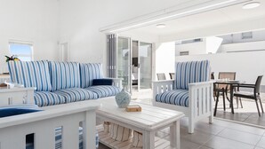 A modern living room with striped blue and white sofas, a white coffee table, and a dining area with a table and chairs. - Lampiesbaai Beach House (Saint Helena Bay)
