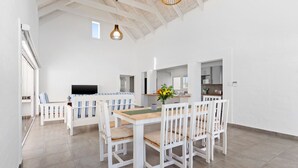 A spacious room with a high ceiling, white walls, and a wooden dining table with white chairs. - Lampiesbaai Beach House (Saint Helena Bay)