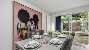 A dining room with a large abstract painting, a table set for four, and a view of the backyard through glass doors.