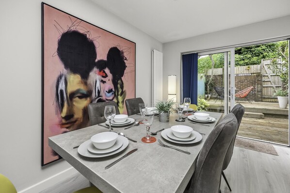 Uma sala de jantar com uma grande pintura abstrata, uma mesa posta para quatro pessoas e vista para o quintal através de portas de vidro.