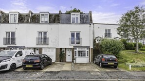 A row of terraced houses with a white facade, a front door, and a small garden area.