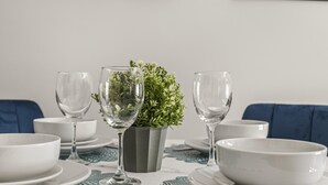 A dining table set with white plates, bowls, and clear wine glasses, centered with a potted plant. - Buzzing Brighton Apartment 4 | By My Getaways (Brighton)