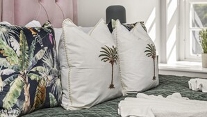 A bed with a green quilt, white pillows with palm tree designs, and a pink headboard. - Buzzing Brighton Apartment 4 | By My Getaways (Brighton)
