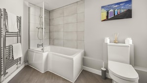 A modern bathroom with a glass-enclosed shower, a white bathtub, and a toilet. - Buzzing Brighton Apartment 4 | By My Getaways (Brighton)