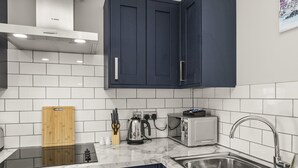 A modern kitchen with dark blue cabinets, white tiled backsplash, a stainless steel sink, a toaster, and a kettle. - Buzzing Brighton Apartment 5 | By My Getaways (Brighton)