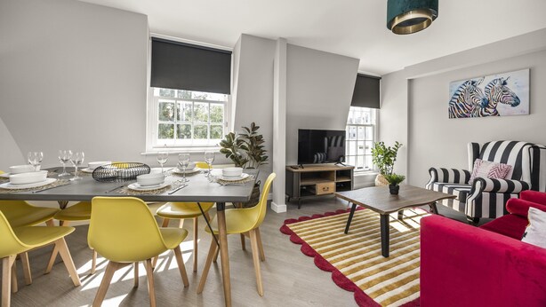 A modern living room with a dining area, a striped sofa, and a television. - Buzzing Brighton Apartment 5 | By My Getaways (Brighton)