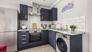 A modern kitchen with dark blue cabinets, a stainless steel refrigerator, a built-in oven, a washing machine, and a tiled backsplash. - Buzzing Brighton Apartment 5 | By My Getaways (Brighton)