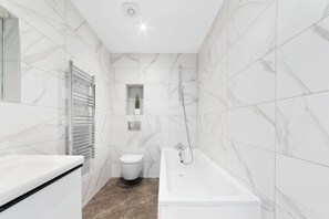 A modern bathroom with a white bathtub, a toilet, and a towel rack.