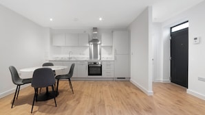 A modern kitchen with white cabinets, a stainless steel range hood, and a built-in oven. - Guest Ready - Oak Crescent City House, London, E14 (London)