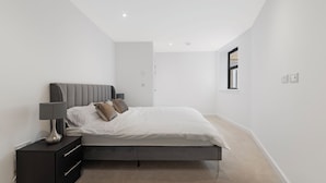 A modern bedroom with a bed, bedside table, and lamp. - Guest Ready - Oak Crescent City House, London, E14 (London)