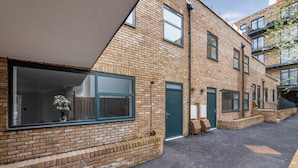 A modern brick building with large windows and a green door. - Guest Ready - Oak Crescent City House, London, E14 (London)